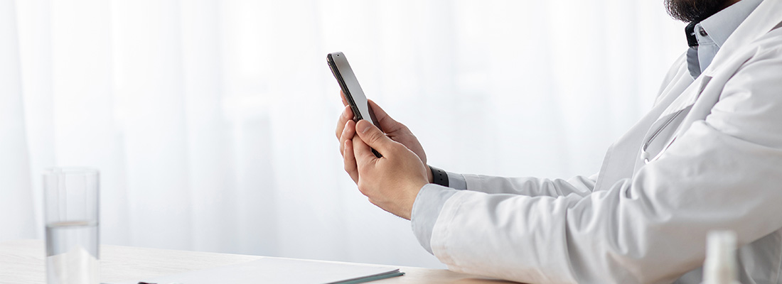 Physician in a white coat using a smartphone at a desk