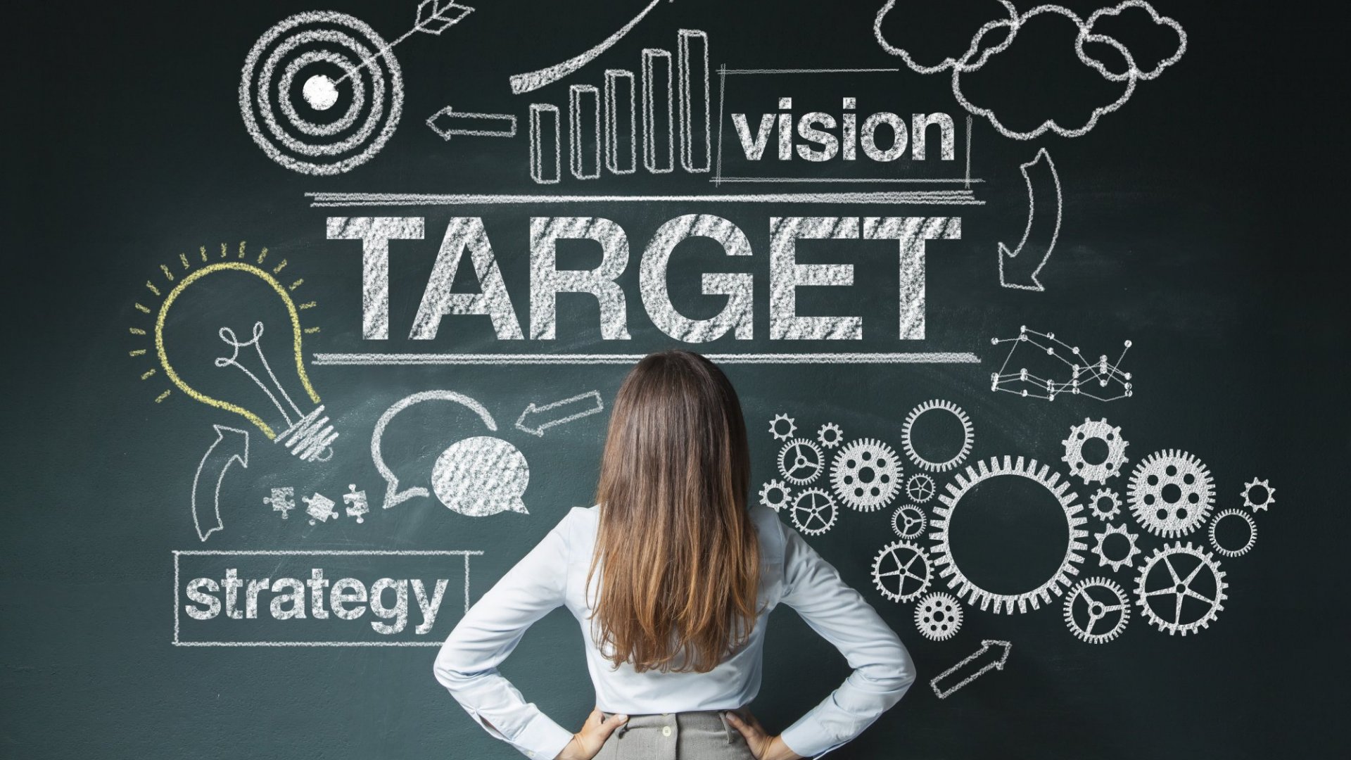 Woman facing a chalkboard sketch of vision, target and strategy